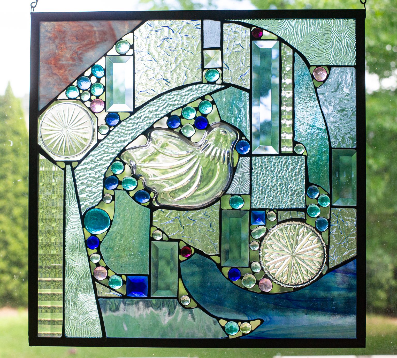 The symbol of peace in the middle of this stained glass window, the sky stained in the upper left corner by the smoke stack beneath it, the ocean waves rising in the right corner and the different shades of blue that represent the one sky that binds us all together.