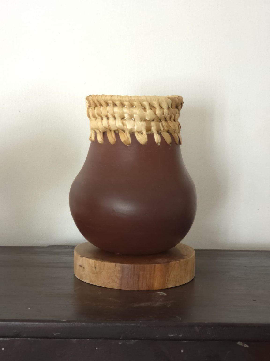 "This vessel celebrates Barbadian natural heritage and artisanal synergy. Hand-sculpted from local clay, it connects to the island's soil. A cane fiber rim honors regional flora, while a Barbadian mahogany base highlights sustainable materials and Commonwealth Resilience."